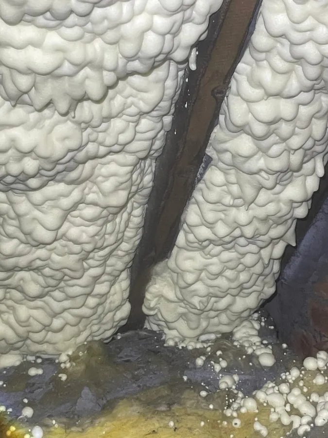 Independent spray foam loft inspection — close-up of closed-cell spray foam encapsulating a rafter, with uneven coverage and drips at the wall plate
